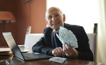 happy senior businessman holding money in hand while working on laptop at table